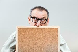 Nerdy businessman is thinking about something while holding empty cork board photo