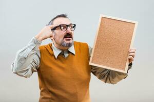 Nerdy businessman is thinking about something while holding empty cork board photo