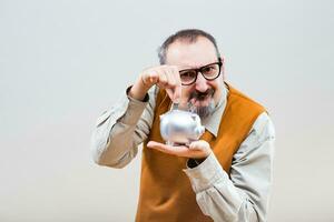 Nerdy man is putting coin into piggy bank photo
