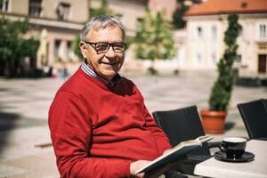 Senior man enjoys reading book and drinking coffee at the bar photo