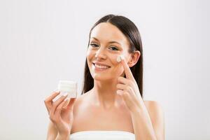 Beautiful woman applying moisturizer on face photo