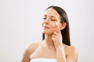 Beautiful woman applying moisturizer on face photo