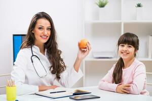 Portrait of child and female doctor holding apple at the medical office photo