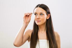 Image of beautiful brunette woman plucking eyebrows photo