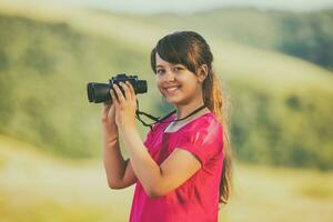 Beautiful little girl enjoys in nature with binoculars photo