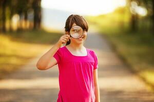 Beautiful little girl looking through magnifying glass in the nature photo