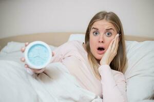 Terrified woman holding alarm clock photo