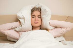 Angry woman disturbed with a noise trying to sleep and covering her ears with a pillow photo