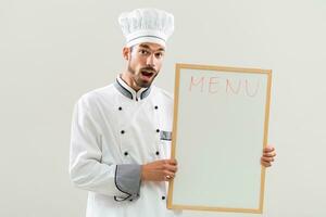 Excited chef is holding whiteboard on gray background photo