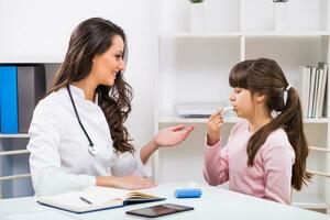 Female doctor showing how to use inhaler to a child at the medical office photo