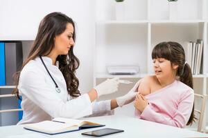 hembra médico dando inyección a un asustado niño a médico oficina foto