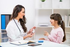 Female doctor showing how to use inhaler to a child at the medical office photo