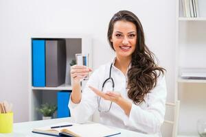 Beautiful female doctor showing glass of water while sitting at her office photo