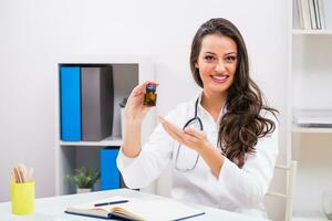 Beautiful female doctor showing bottle of capsule while working at her office photo