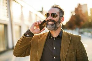 Modern businessman with beard using mobile phone while standing on the city street photo
