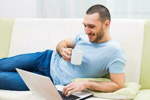 Young man using laptop and drinking coffee at his home photo