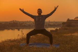 hombre haciendo yoga en puesta de sol con ciudad ver foto