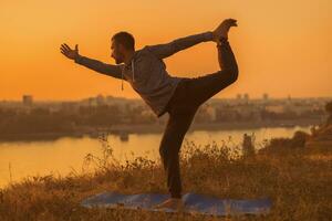 Man doing yoga on sunset with city view photo