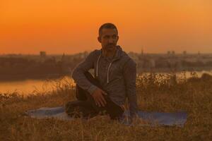 hombre haciendo yoga en puesta de sol con ciudad ver foto