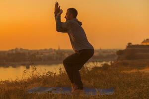 hombre haciendo yoga en puesta de sol con ciudad ver foto