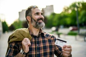 Portrait of modern businessman with beard holding credit card while standing on the city street photo