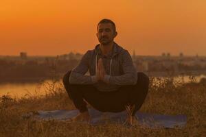 hombre haciendo yoga en puesta de sol con ciudad ver foto