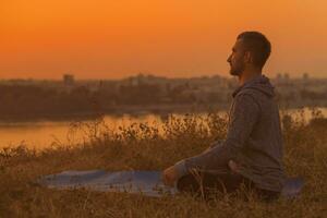 Man doing yoga on sunset with city view photo