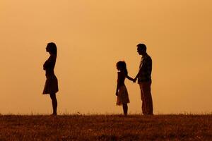 Silhouette of a angry wife turning back while her husband and daughter are looking at her photo