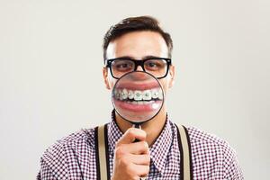 Nerdy man is showing his braces with magnifying glass photo