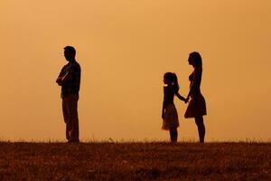 Silhouette of a angry husband turning back while his wife and daughter are looking at him photo