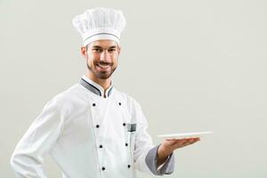 Smiling chef is holding plate and  on gray background. photo