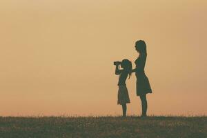 Little girl is standing with her mother outdoor and watching with binoculars nature. photo