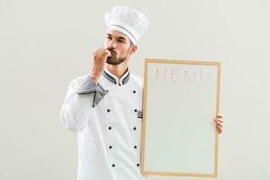Chef is showing delicious sign and whiteboard on gray background photo