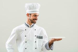 Smiling chef is holding plate and  on gray background. photo