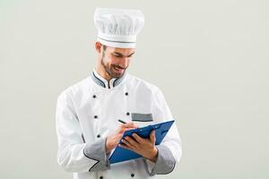 Smiling chef is holding cookbook and writing a new recipe photo