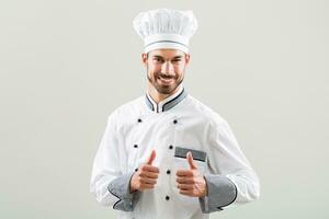 Smiling chef showing thumb up on gray background. photo