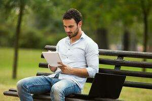 Young businessman is sitting at the park and working photo