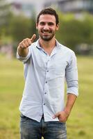 Young businessman is standing in the park and showing thumb uP photo