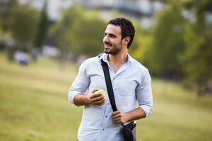 Young businessman is eating apple at the park photo