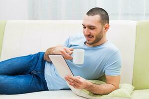 Young man using digital tablet and drinking coffee at his home photo