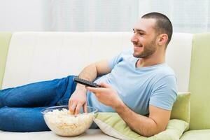 joven hombre disfruta acecho televisión y comiendo palomitas de maiz foto