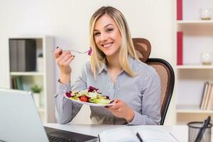 hermosa mujer de negocios disfruta comiendo ensalada mientras trabajando en su oficina foto