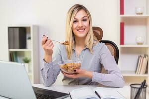 Beautiful businesswoman enjoys eating corn flakes for breakfast while working in her office. photo