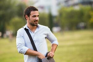 Young businessman standing at the park and searching something in his bag photo