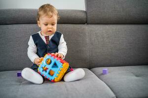 Cute little baby boy playing with toys while sitting on sofa photo