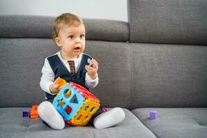 linda pequeño bebé chico jugando con juguetes mientras sentado en sofá foto