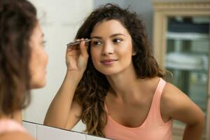 Beautiful woman plucking eyebrows in bathroom photo