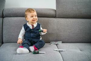 Cute little baby boy playing with toys while sitting on sofa. photo