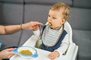 Cute baby boy learning to  eat by himself while sitting in a high chair photo