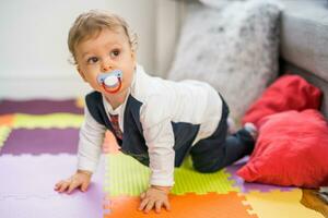 Image of cute baby boy with pacifier crawling on the floor photo